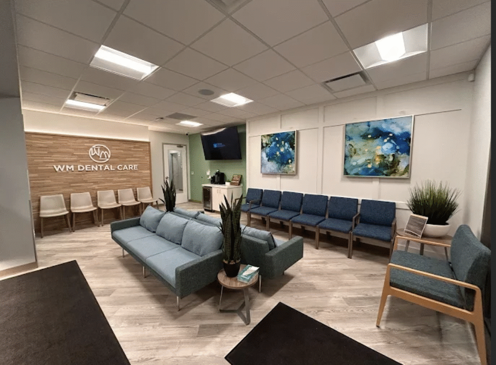 Dental office interior featuring modern seating, WM Dental Care logo on wooden wall, vibrant artwork, and a welcoming atmosphere in Hamburg.